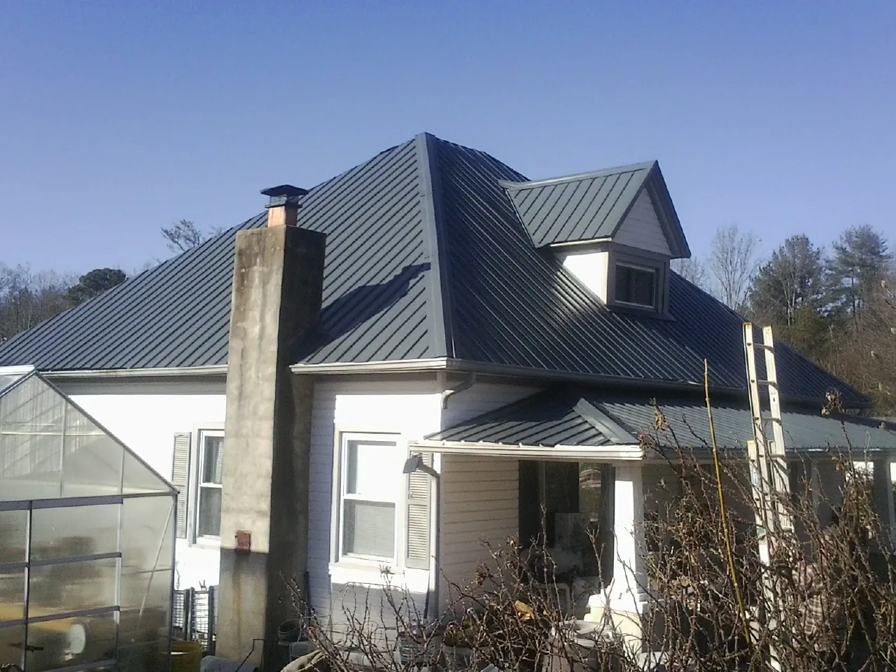 Dark blue standing seam metal roof on a white farmhouse with dormer — Slate & Tile Roof Repair by Roofing Brothers in Tennessee Colony