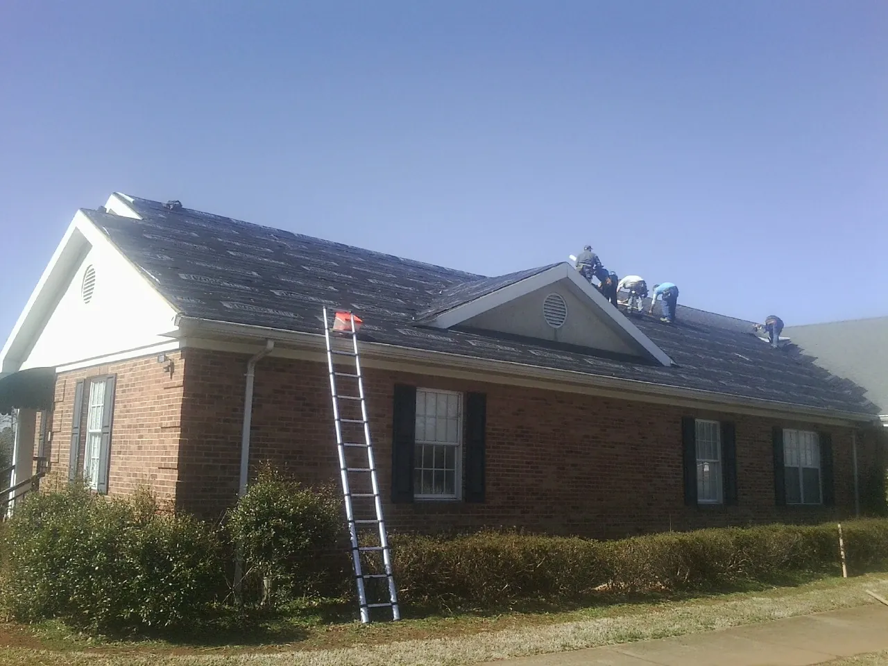Crew tearing shingles off a brick ranch roof with a ladder set — Metal Roof Repair work by our crew in Tennessee Colony