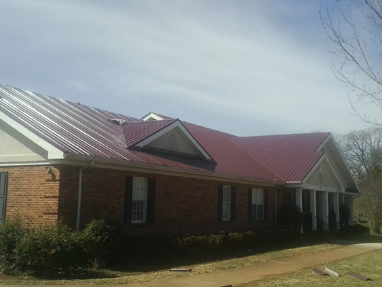 Red metal roof with gabled entries on a long brick building, from a Hail Damage Roof Repair job in Tennessee Colony