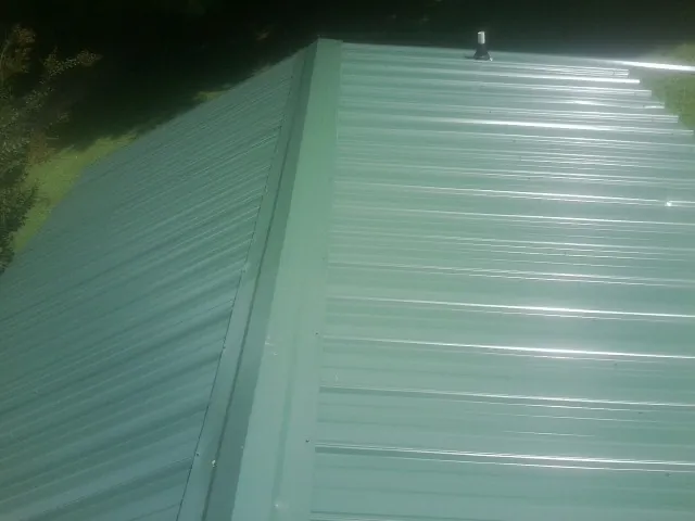 New green metal panels meeting at the ridge of a roof — Flat Roof Repair work by our crew in Tennessee Colony