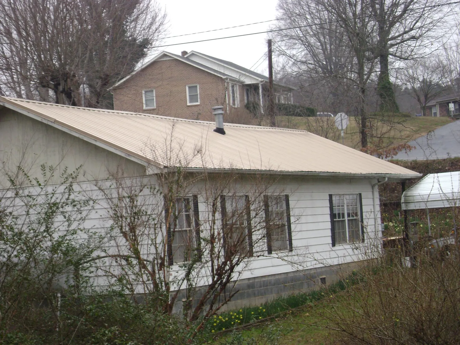 Tan metal roof on a white sided house set into a hillside — Commercial Roofing by Roofing Brothers in Tennessee Colony