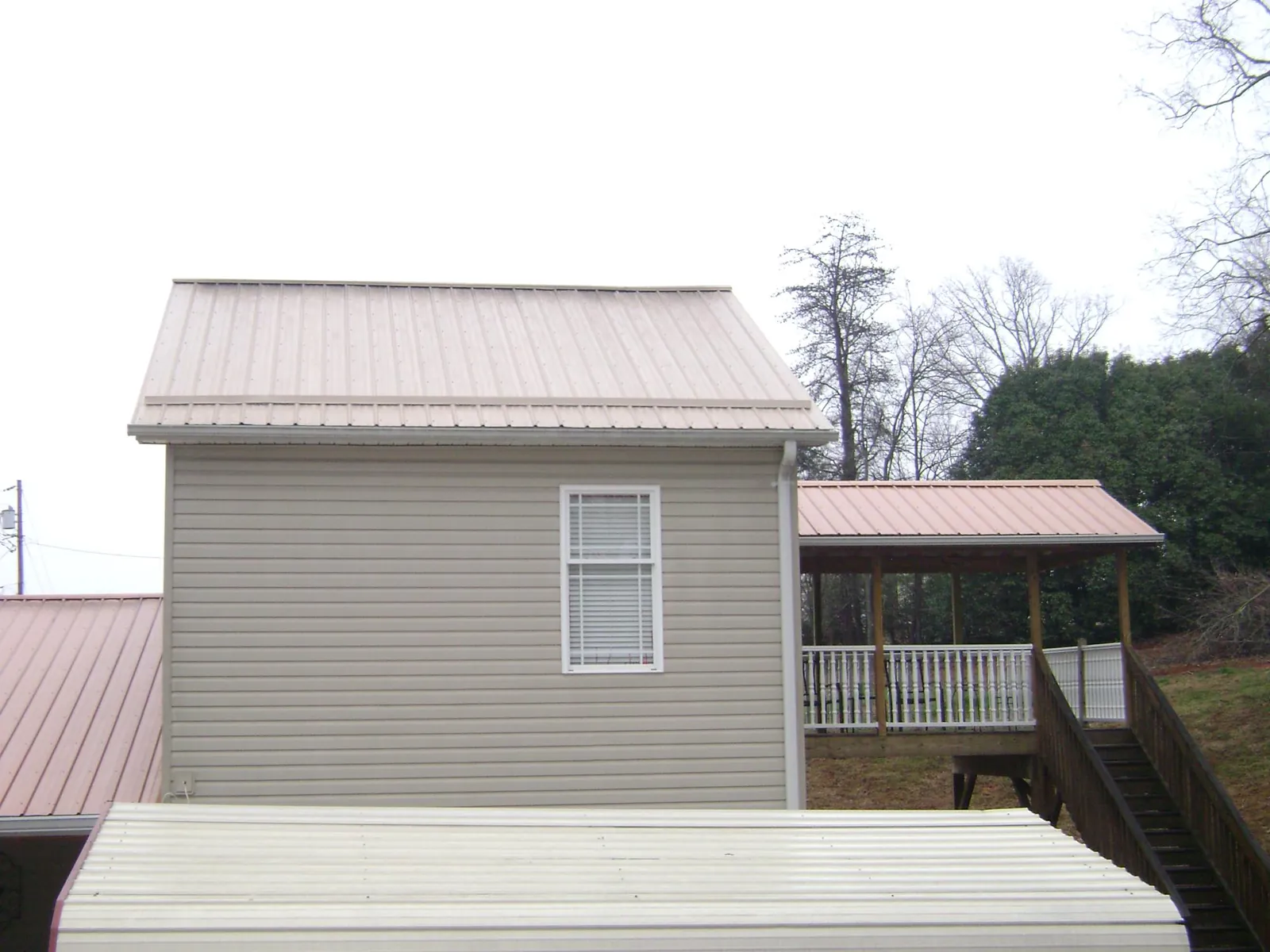 Tan metal roofs on a two story addition and attached porch, from a Roof Replacement job in Tennessee Colony
